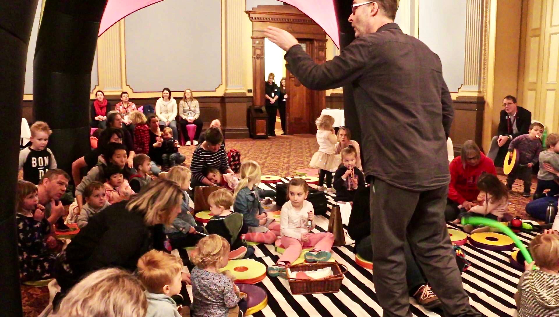 A man directing a grouped of seated toddlers with instruments